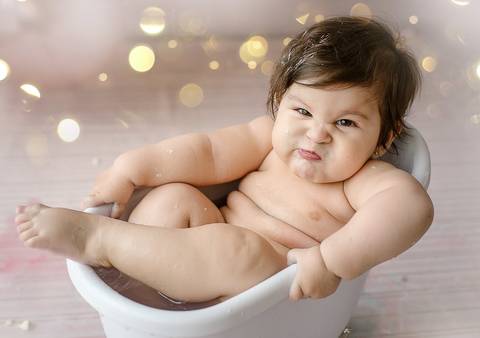 Bebê em ensaio Smash the Cake sentada em banheira branca, expressão divertida, fotografia infantil em estúdio em Farroupilha.'