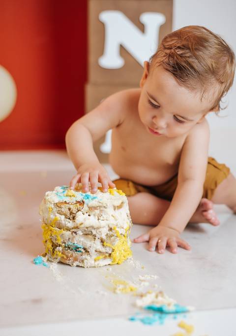 Bebê observando as próprias mãos após tocar o bolo no Smash the Cake, fotografia infantil de 1 ano.'