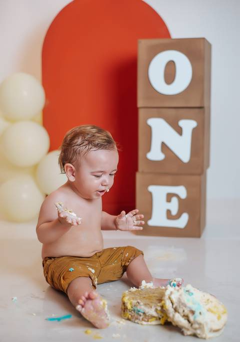 Bebê com as mãos sujas de bolo no ensaio Smash the Cake, fotografia infantil espontânea e divertida.'