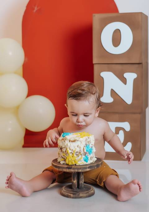 Ensaio Smash the Cake com bebê explorando a cobertura do bolo, registro de fotografia infantil focado na experiência do momento.'