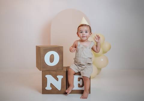 Bebê de 1 aninho sorrindo em ensaio infantil com elementos neutros'