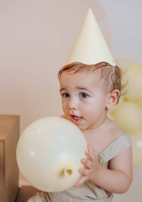 Close de bebê de 1 aninho interagindo com balão claro durante ensaio fotográfico infantil'