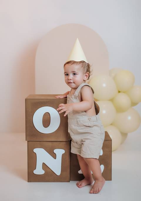Bebê de 1 ano apoiado em cubo com a letra O em ensaio de aniversário em estúdio'