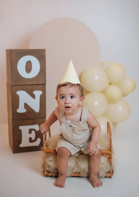 Ensaio de 1 aninho com bebê em pé ao lado de cubos ONE e balões em cenário neutro'