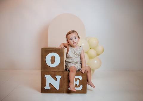 Ensaio de 1 aninho com bebê sentado sobre cubos de madeira e fundo neutro'