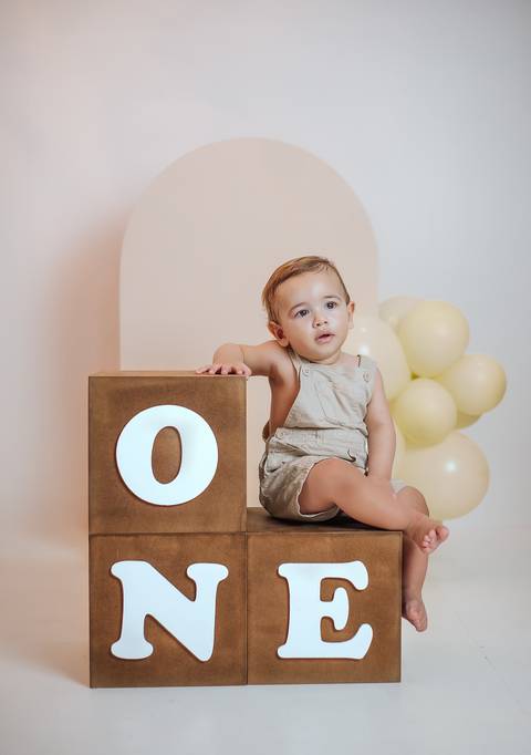Bebê de 1 ano apoiado em cubo decorativo durante ensaio infantil em estúdio'