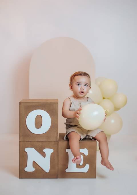 Ensaio infantil de 1 ano com bebê interagindo com balão em cenário minimalista'