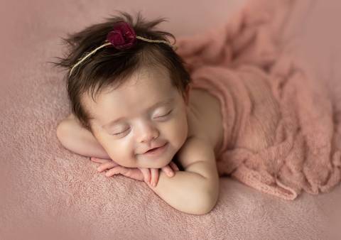 Bebê old newborn de 3 meses apoiada de bruços em cenário rosado, posição confortável e segura'