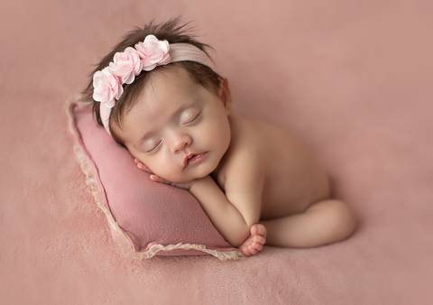 Bebê old newborn de 3 meses usando touca rosa, posição lateral confortável em estúdio'