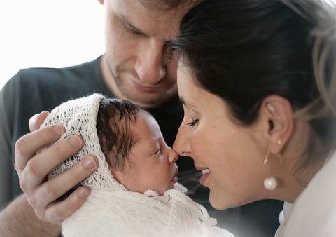 Ensaio newborn com o Ravi recém-nascido no colo dos pais, close afetivo destacando vínculo familiar'