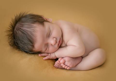 Bebê recém-nascido em ensaio newborn tradicional, deitado de lado em cenário neutro e iluminação suave'