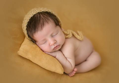 Ensaio newborn tradicional com bebê recém-nascido apoiado sobre almofada, posição confortável e segura'