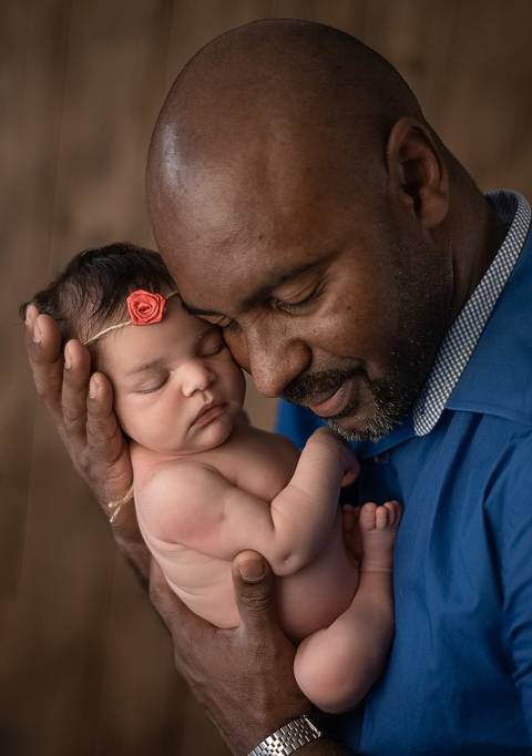 Fotografia newborn tradicional com bebê recém-nascida no colo do pai, registro familiar delicado'