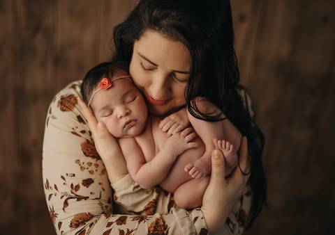 Fotografia newborn com bebê recém-nascida no colo da mãe, registro de vínculo familiar em estúdio'