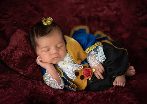 Bebê recém-nascido em ensaio newborn temático A Bela e a Fera, figurino azul e dourado em estúdio'