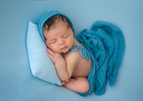 Fotografia newborn de recém-nascido deitado sobre almofada, iluminação suave e condução técnica'