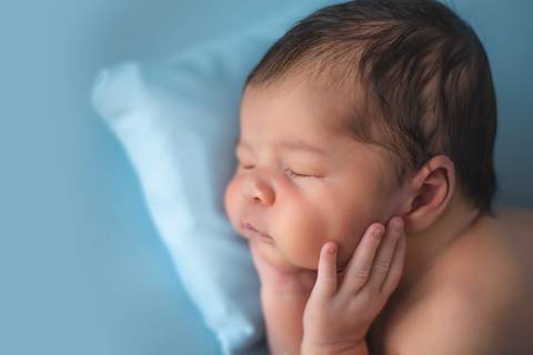 Bebê recém-nascido em ensaio newborn tradicional, close lateral destacando traços do bebê'