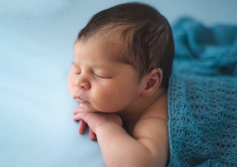 Fotografia newborn tradicional com bebê recém-nascido deitado de lado, cenário azul claro em estúdio'