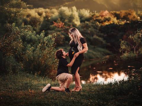 Mulher grávida em ensaio gestante ao ar livre, acompanhada do filho mais velho, em ambiente natural. Imagem que retrata o vínculo familiar durante a gestação.'