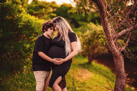 Mulher grávida em ensaio gestante na natureza, acompanhada do filho, caminhando entre árvores, com foco na relação entre maternidade e gestação.'