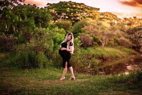 Mulher grávida em ensaio gestante sozinha, em ambiente natural próximo à água, destacando a silhueta e a barriga em evidência.'
