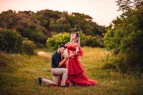 Mulher grávida em ensaio gestante com o companheiro, em ambiente natural, com ambos interagindo com a barriga, representando a construção da família.'