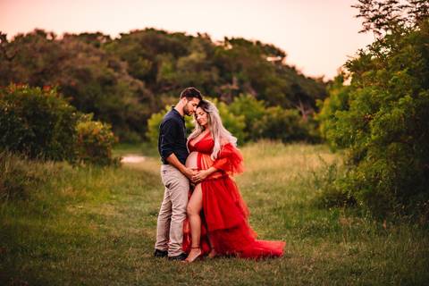 Mulher grávida em ensaio gestante com o companheiro, ambos de pé em ambiente natural, interagindo com a barriga, representando a espera pelo bebê.'