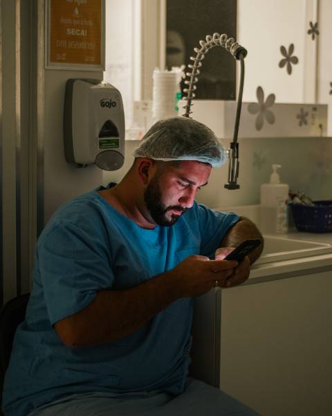 Pai aguardando o nascimento do filho no Hospital Tacchini, vestido com roupas hospitalares, em momento de expectativa antes do parto.'