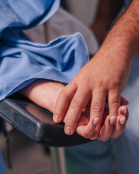 Mãos do pai segurando a mão da mãe durante o trabalho de parto hospitalar em Bento Gonçalves.'