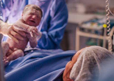 Recém-nascido sendo pesado e avaliado pela equipe médica após o parto no Hospital Tacchini.'