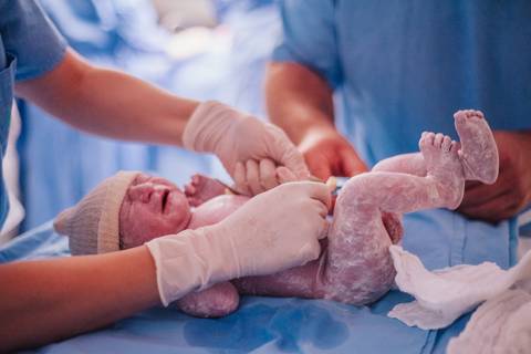 Recém-nascido sendo pesado e avaliado pela equipe médica após o parto no Hospital Tacchini.'