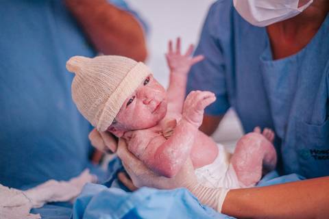 Recém-nascido sendo apresentado à mãe momentos após o parto hospitalar, ainda com sinais do nascimento.'