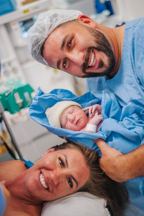 Pai segurando o recém-nascido pela primeira vez após o parto hospitalar, em momento de acolhimento.'