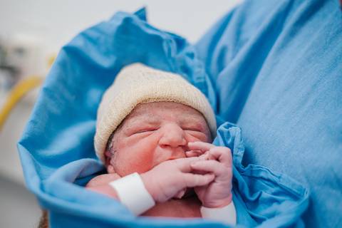 Recém-nascido enrolado em tecido hospitalar, minutos após o nascimento, em ambiente de parto.'