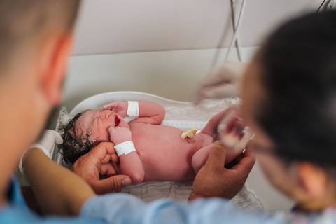 Recém-nascido sendo avaliado pela equipe médica após o nascimento, ainda no centro obstétrico.'