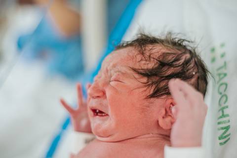 Recém-nascido chorando nos primeiros minutos de vida, logo após o nascimento em ambiente hospitalar.'