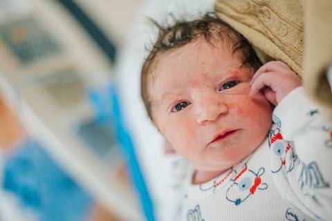 Recém-nascido acordado no berço hospitalar, sendo observado logo após o nascimento.'