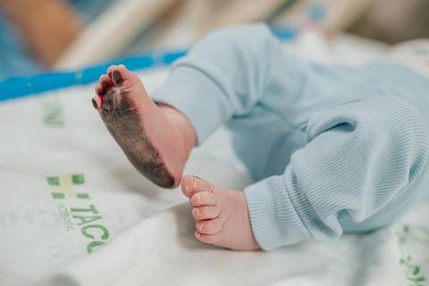 Detalhe dos pés do recém-nascido sobre o lençol hospitalar, minutos após o parto.'