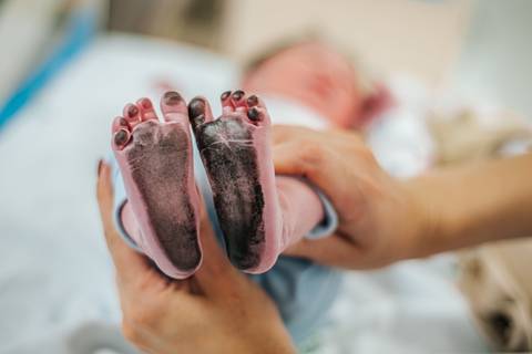 Detalhe dos pés do recém-nascido segurados por um adulto, em registro de nascimento hospitalar.'