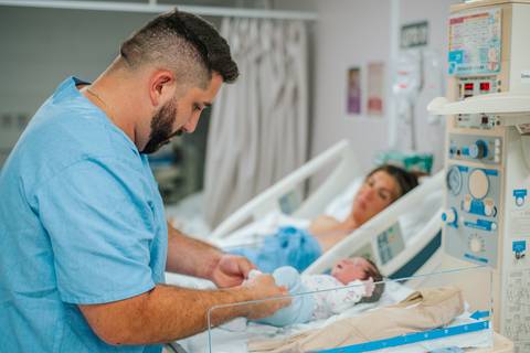 Pai acompanhando os primeiros cuidados com o recém-nascido no quarto hospitalar após o parto.'