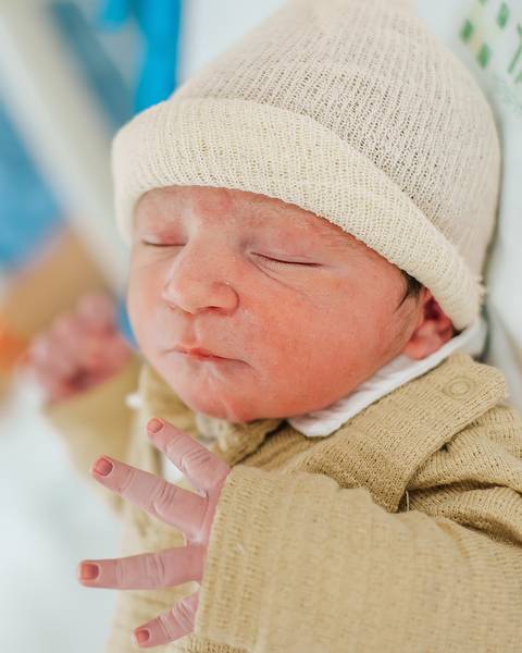 Recém-nascido dormindo, usando touca, em registro delicado dos primeiros dias de vida.'