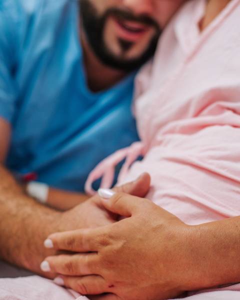 Mãe em trabalho de parto no Hospital Tacchini de Bento Gonçalves, com mãos apoiadas na barriga durante o processo de nascimento.'