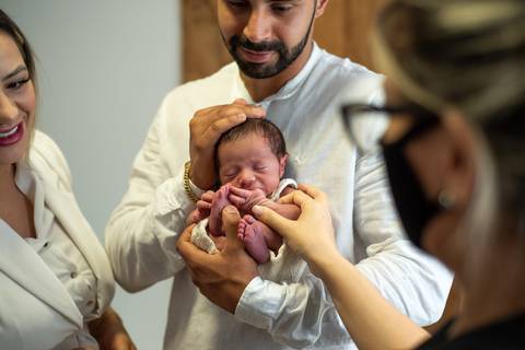 Pais segurando o recém-nascido com orientação da mentoria newborn conduzida por Aline Fontes para Priscilla Patzlaff, fotógrafa newborn em Bento Gonçalves.'