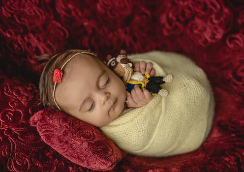 Bebê de 45 dias em ensaio old newborn, envolta em tecido claro e apoiada em cenário vermelho, posição segura e confortável'