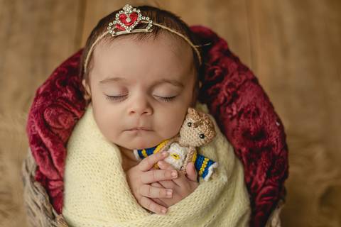 Bebê old newborn de 45 dias apoiada em almofada, cenário vermelho e iluminação suave, ensaio adaptado para bebê fora do período newborn tradicional'