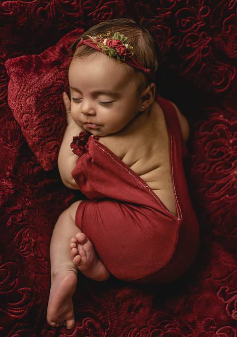 Fotografia old newborn de bebê com 45 dias envolta em tecido vermelho, posição lateral confortável respeitando os limites do bebê'