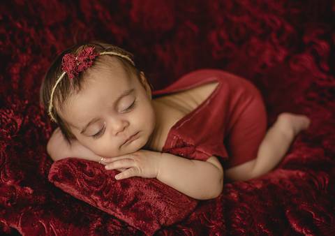 Fotografia old newborn de bebê com 45 dias apoiada de bruços em cenário vermelho, posição confortável e segura'