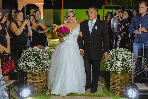 noiva entrando com seu pai, desfilando pela linda passarela de flores com seu vestido de noiva deslumbrante.'