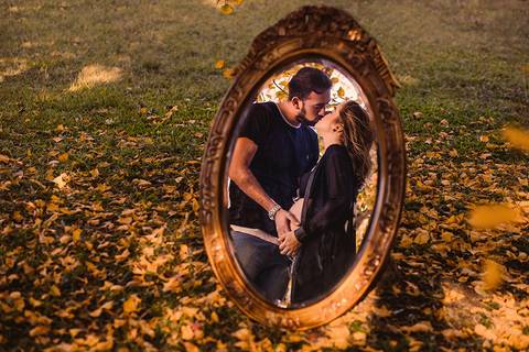 Retrato criativo de casal gestante com espelho e folhas amarelas caídas ao chão'