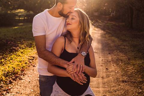 Retrato de casal gestante no contraluz em estrada de chão'